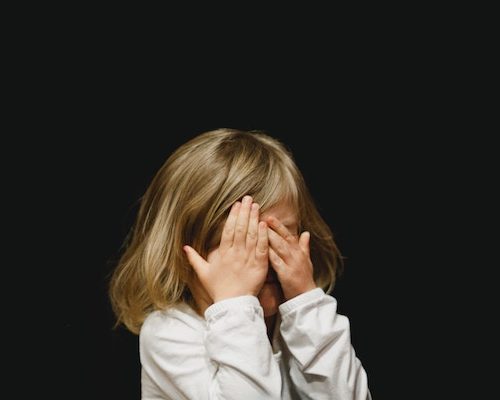 child hiding face with hands